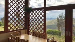Una mesa de comedor de madera con sillas, una ventana con celosía y una planta colgante.