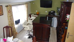 A compact living space with a dining area, a kitchen, and a TV mounted on the wall. - La Maison Celtique Chambres d'hôtes (Saint-Nicolas-du-Pelem)
