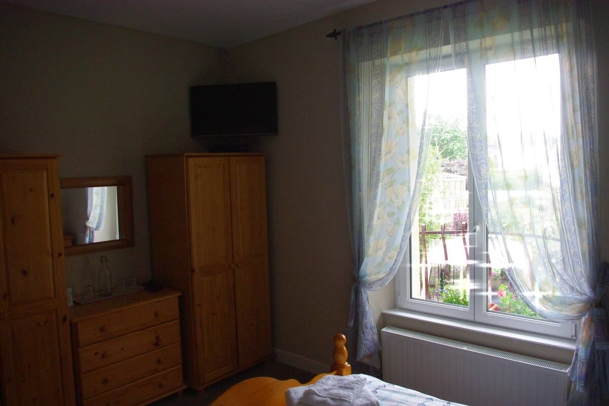 A bedroom with a bed, wooden wardrobe, a television on the wall, and a window with curtains.