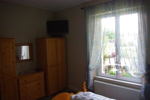 Un dormitorio con cama, armario de madera, televisor en la pared y ventana con cortinas.