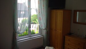 A room with a window, a radiator, a wooden wardrobe, a television, and a mirror. - La Maison Celtique Chambres d'hôtes (Saint-Nicolas-du-Pelem)