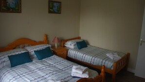 A room with two single beds, each with a wooden headboard, a nightstand, and a lamp. There are two paintings on the wall. - La Maison Celtique Chambres d'hôtes (Saint-Nicolas-du-Pelem)