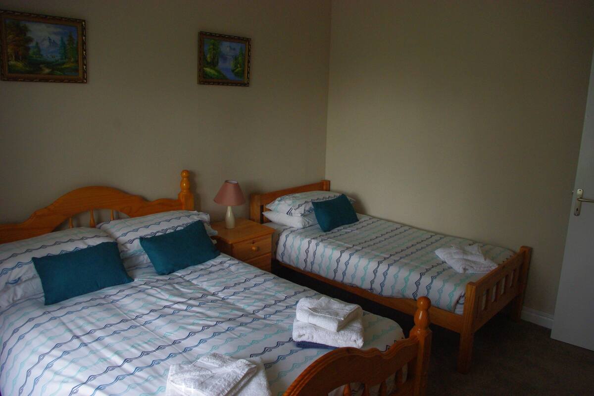 A room with two single beds, each with a wooden headboard, a nightstand, and a lamp. There are two paintings on the wall.