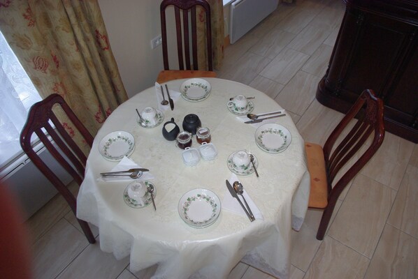 Una mesa de comedor lista con platos, cubiertos y tazas, rodeada de sillas.