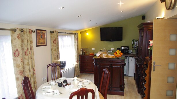 A dining area with a table set for four, a kitchen with a coffee machine, and a television on the wall. - La Maison Celtique Chambres d'hôtes (Saint-Nicolas-du-Pelem)
