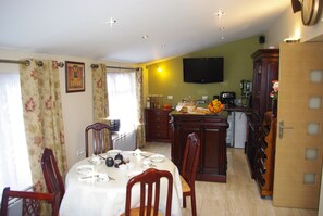 A dining area with a table set for four, a kitchen with a coffee machine, and a television on the wall. - La Maison Celtique Chambres d'hôtes (Saint-Nicolas-du-Pelem)