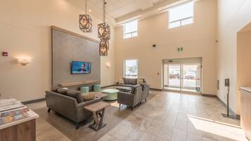 A spacious lobby with a reception desk, comfortable seating, a television, and a large window providing natural light.