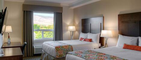 A hotel room with two beds, a desk, and a window with curtains.