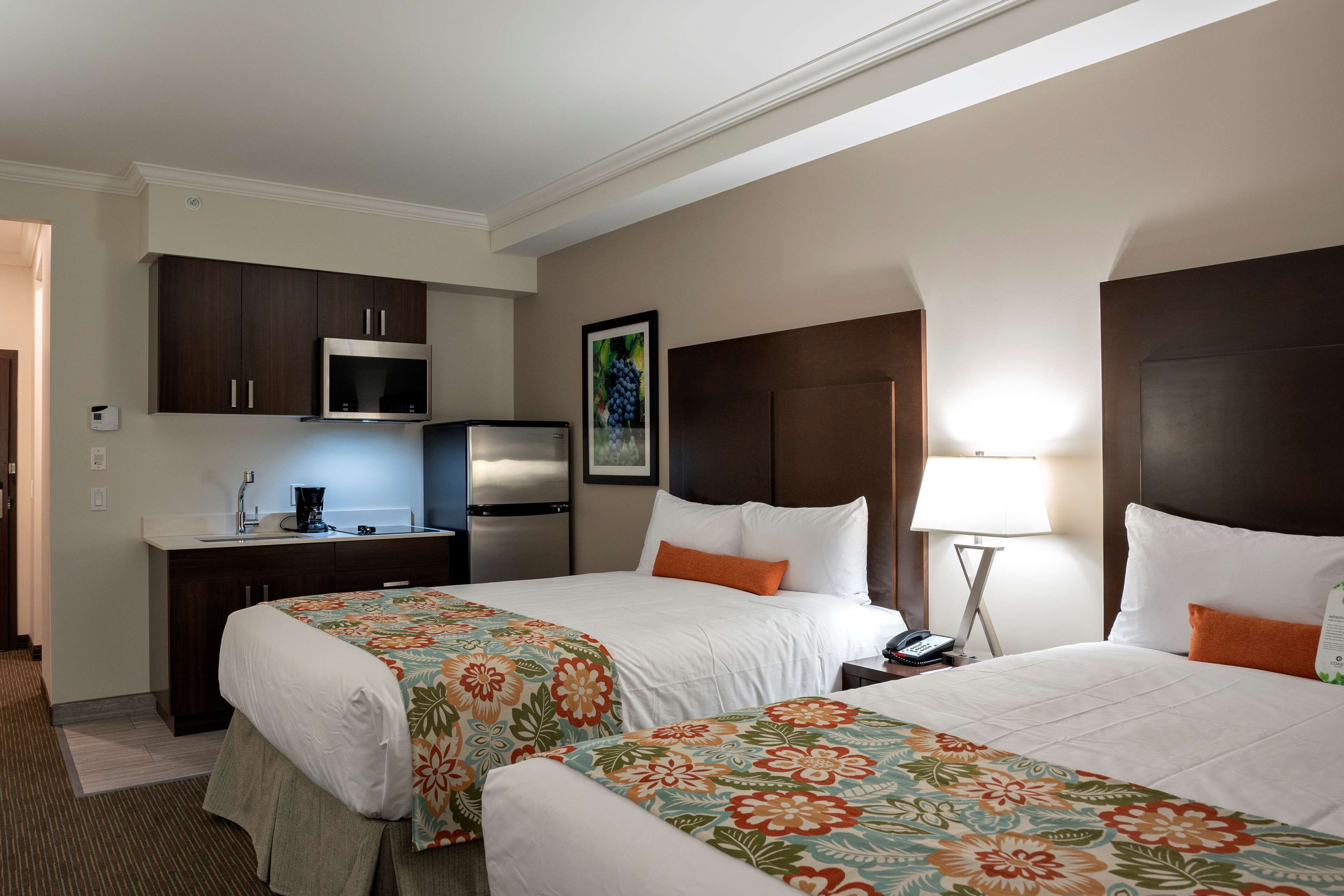 Quarto de hotel com duas camas, uma cozinha compacta e um quadro na parede.