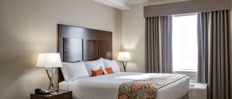 A hotel room with a large bed, two bedside lamps, a nightstand with a phone, a window with curtains, and an air conditioning unit.