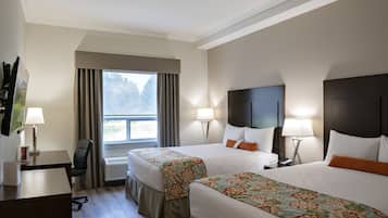 A hotel room with two beds, a desk, and a chair. There is a window with curtains, a lamp, and a TV on the desk.