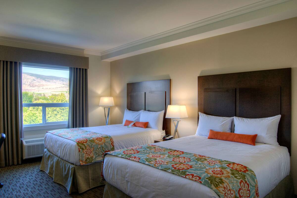 Habitación de hotel con dos camas, un ventanal con cortinas y vistas al exterior.