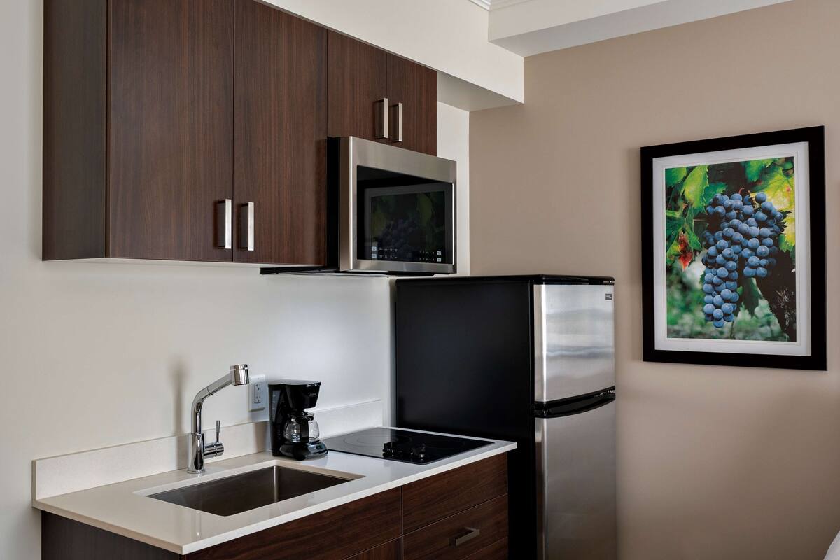 Una cocina moderna con armarios de madera oscura, un refrigerador de acero inoxidable, un microondas y una cafetera.