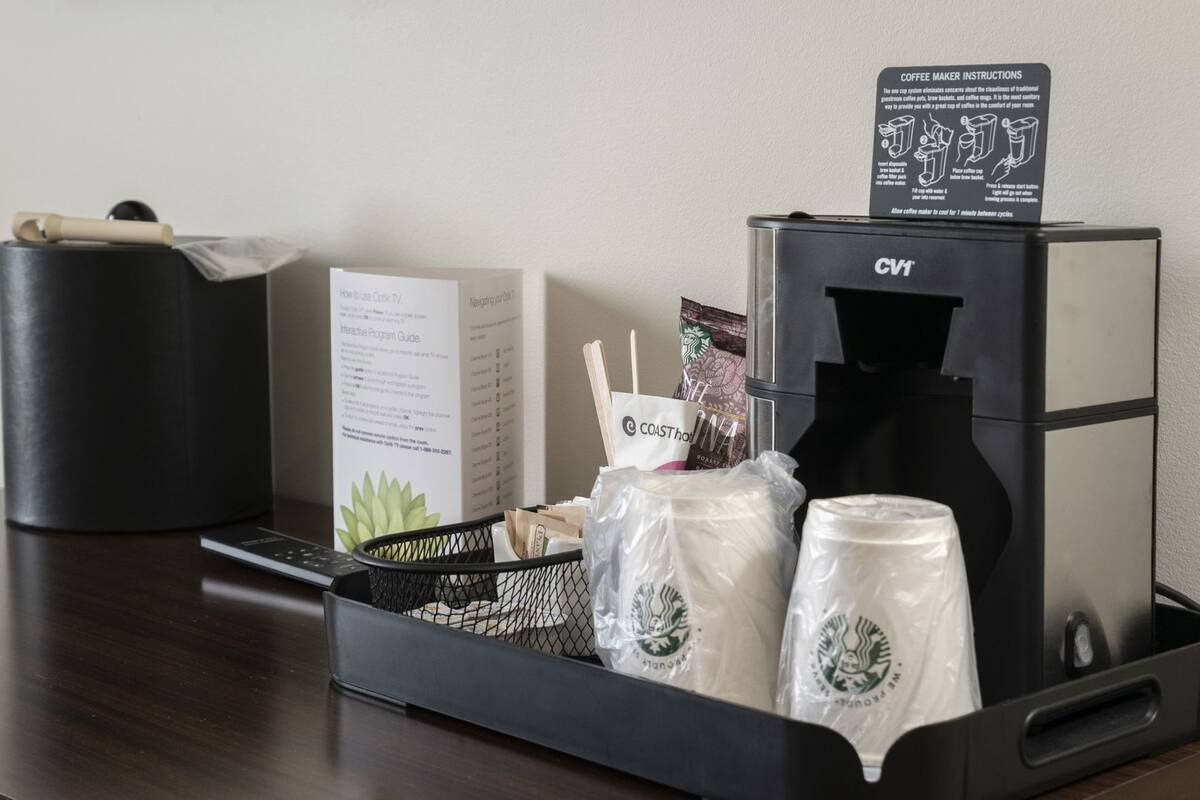 Una cafetera, un control remoto, una caja con la etiqueta 'Guía Interactiva de Programación' y una cesta con bolsas de Starbucks y utensilios.