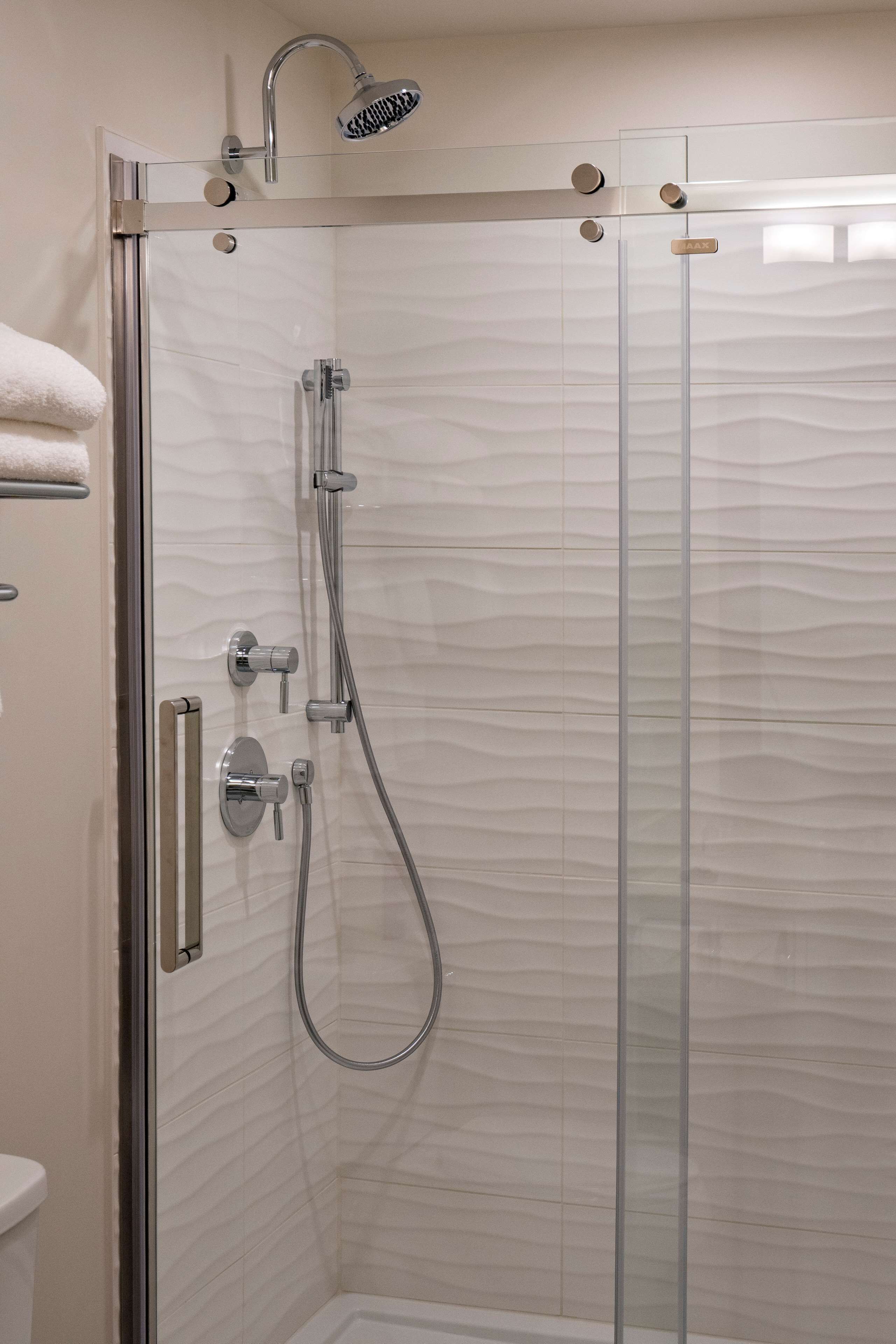 A glass-enclosed shower stall with a handheld showerhead and a wall-mounted faucet.