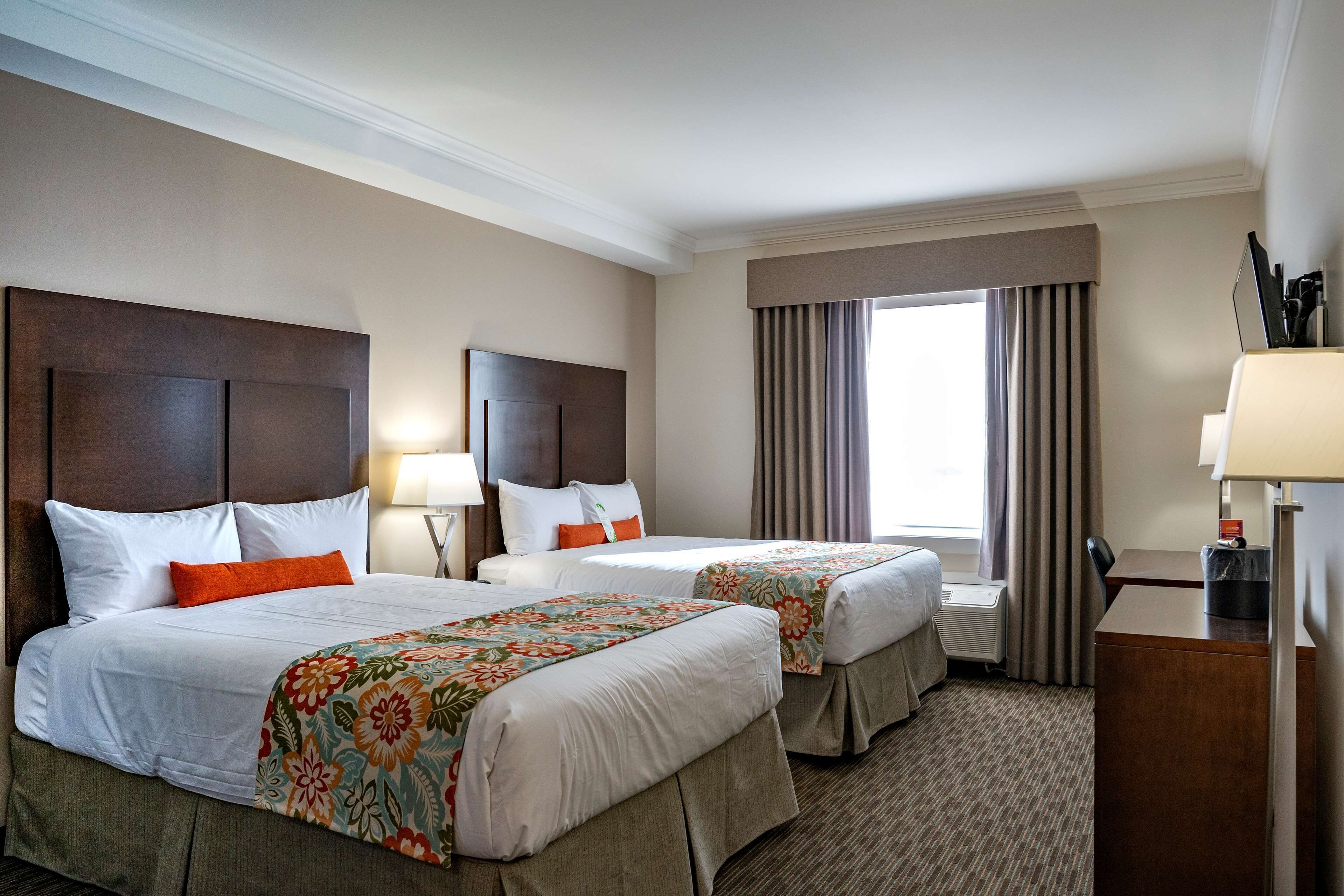 A hotel room with two beds, a desk, and a window with curtains.