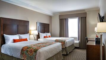 A hotel room with two beds, a desk, and a window with curtains.