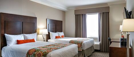 A hotel room with two beds, a desk, and a window with curtains.