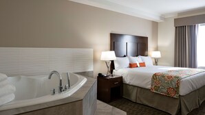 A hotel room with a large bathtub, a bed with white bedding and orange pillows, two bedside lamps, and a floral bedspread. - Coast Oliver Hotel (Oliver)