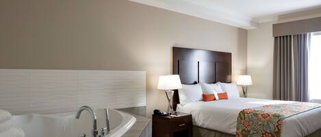 Quarto de hotel com uma banheira grande, cama com roupa de cama branca e almofadas laranja, duas luminárias de cabeceira e um espalhadeira floral.