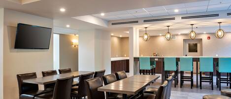Un salón de conferencias con una mesa larga y sillas, un televisor de pantalla plana y una kitchenette con taburetes de bar.