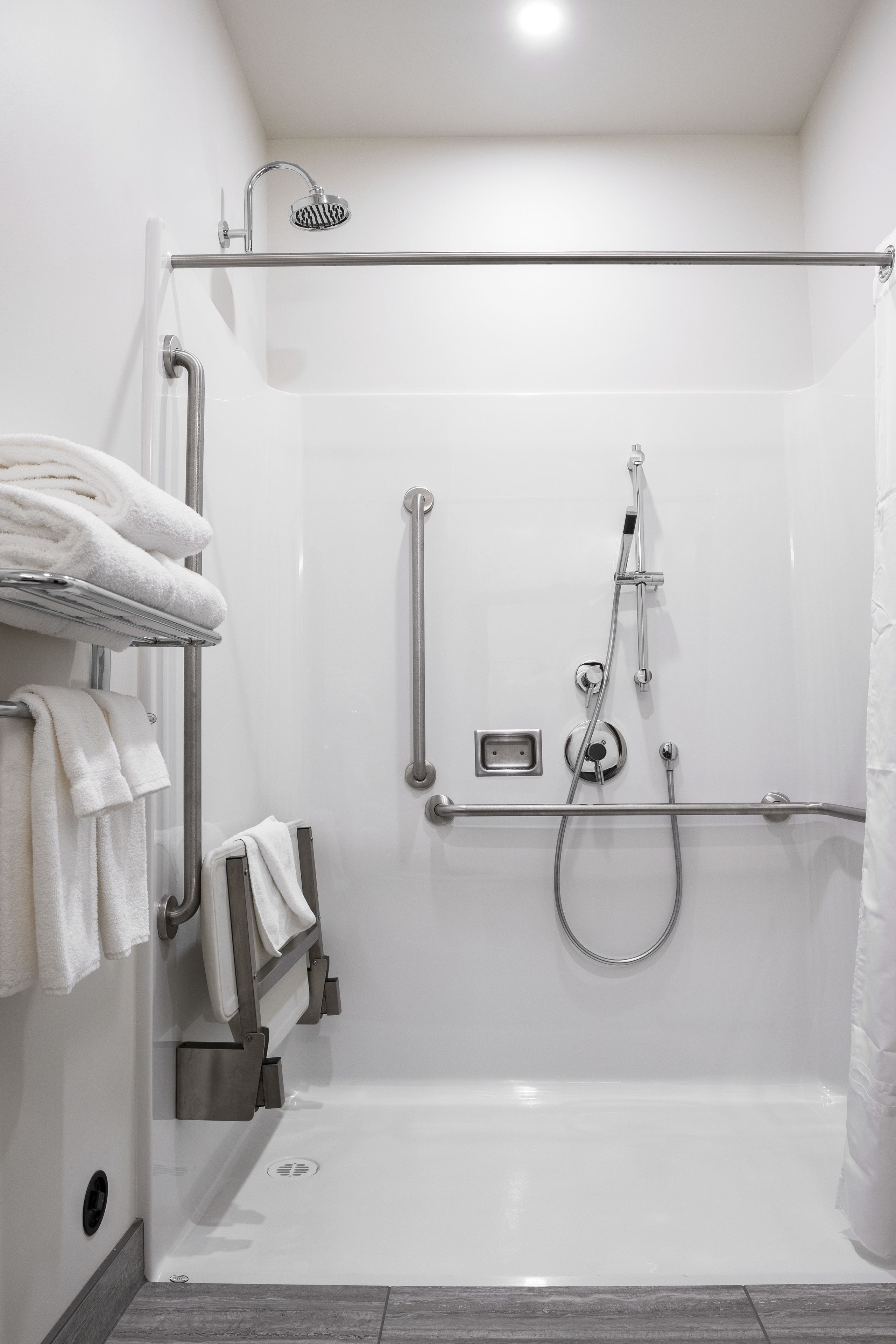 A modern shower area with a glass door, a handheld showerhead, a handheld shower attachment, and a towel rack with folded towels.