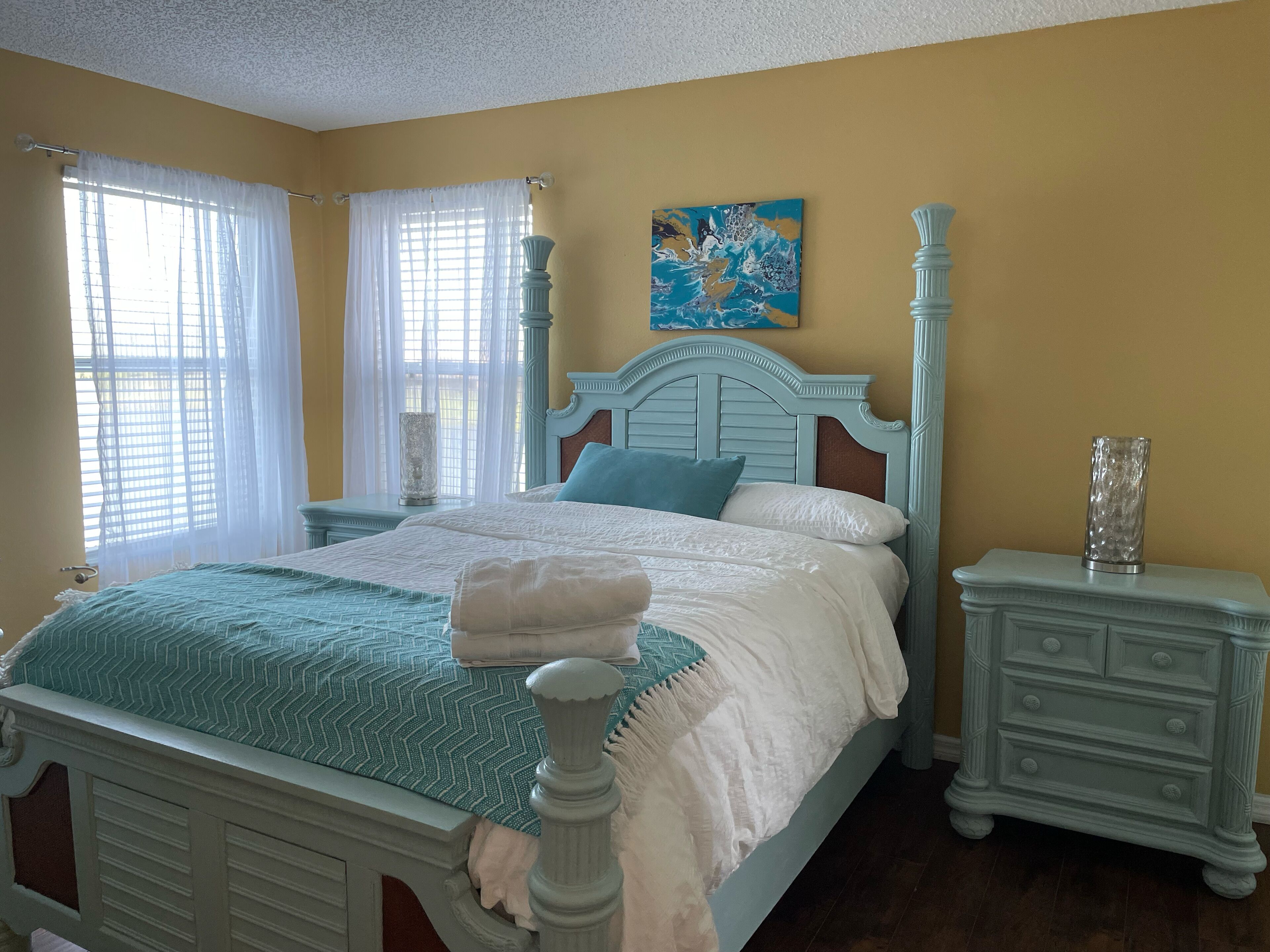 A bedroom with a bed, nightstands, a painting, and a window with curtains.