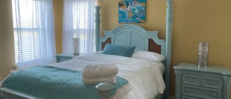 A bedroom with a bed, nightstands, a painting, and a window with curtains.