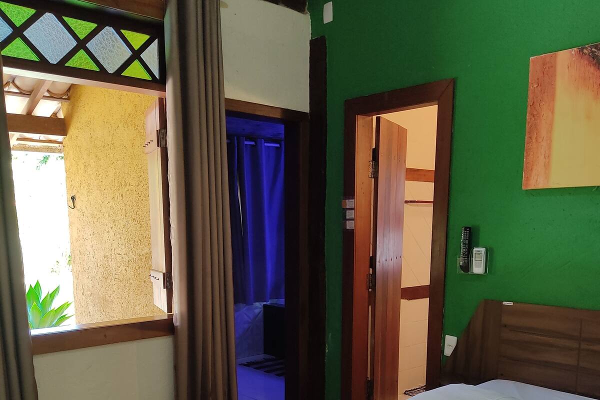 A hotel room with a bed, curtains, a green wall, and a door leading to a bathroom.