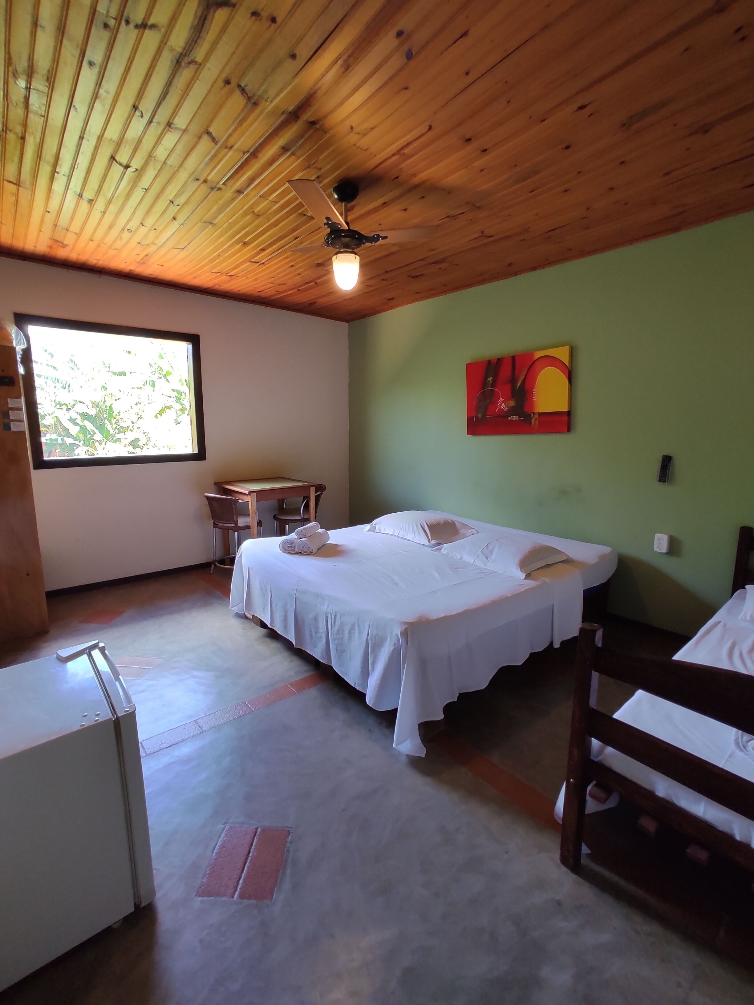 Una habitación con una cama, un escritorio y una silla. Tiene una ventana y un ventilador de techo.