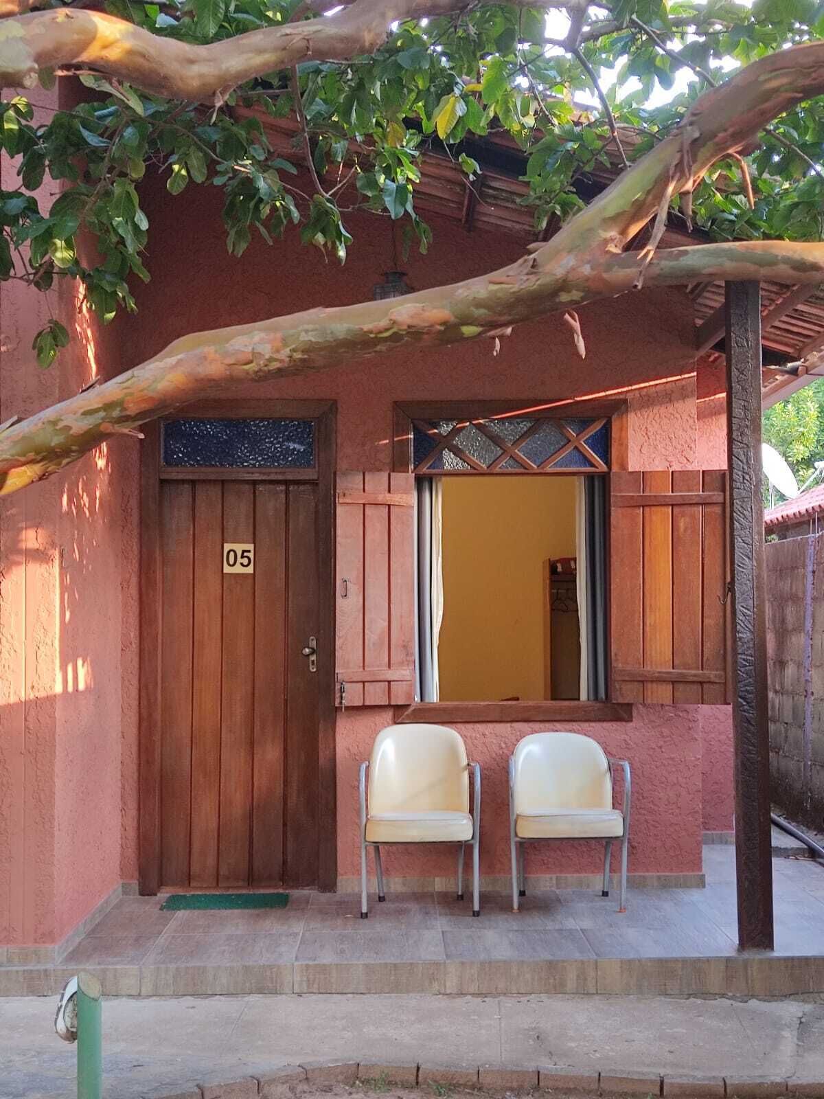 Un edificio con una puerta de madera marcada con el número '05', dos sillas blancas al frente y una ventana con un marco decorativo.