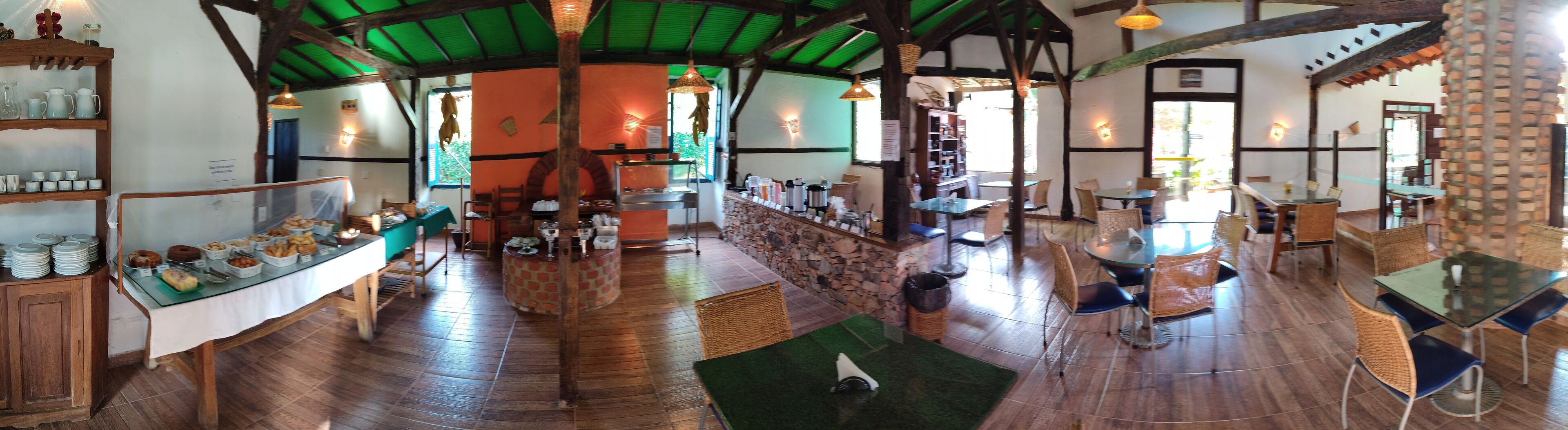 Un restaurant chaleureux avec un plancher en bois, un mur en pierre et un toit végétalisé. On y trouve des tables et des chaises pour les repas, ainsi qu’un buffet proposant divers plats.