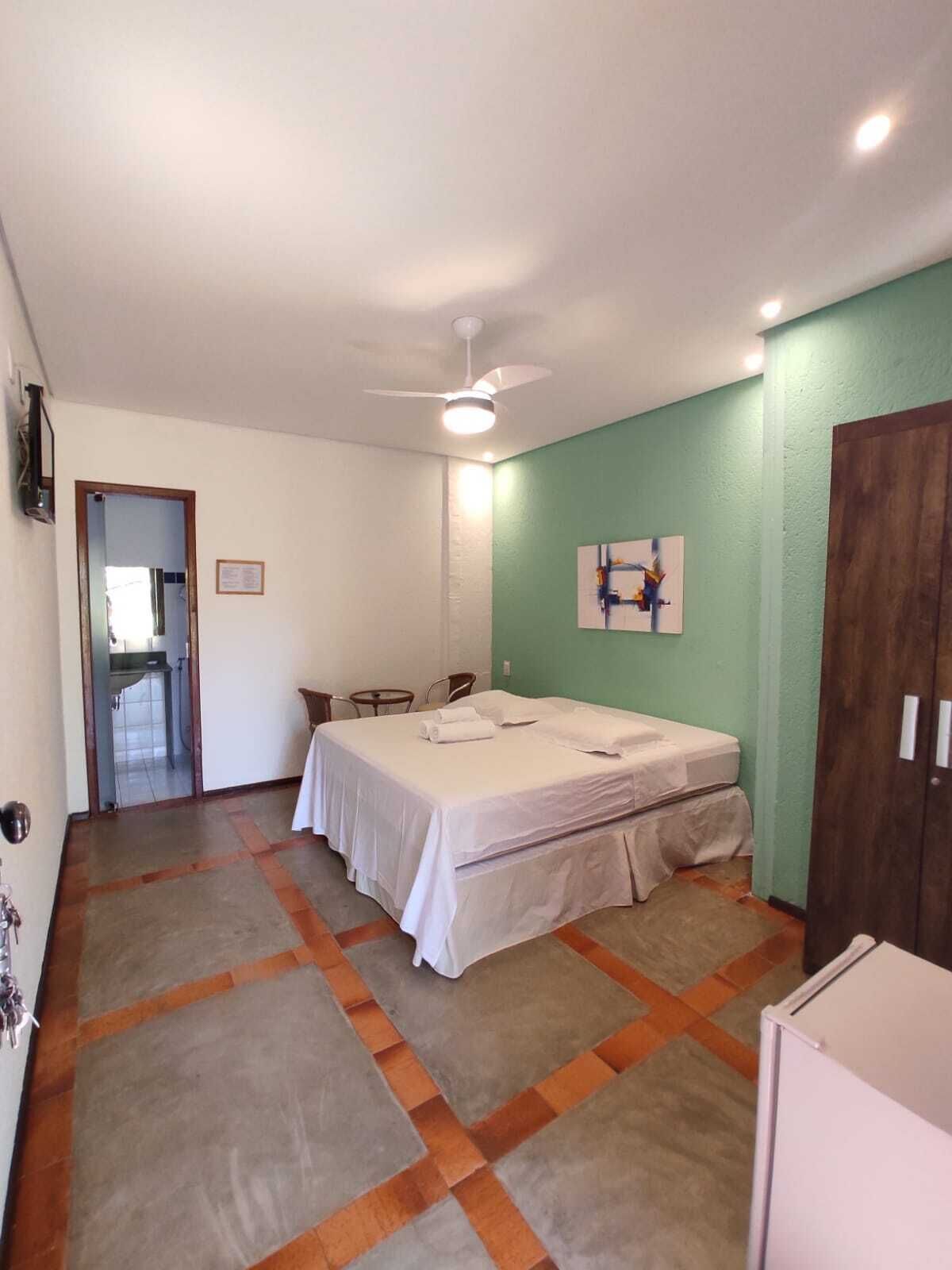 A bedroom with a bed, a ceiling fan, a small table with chairs, and a door leading to another room.