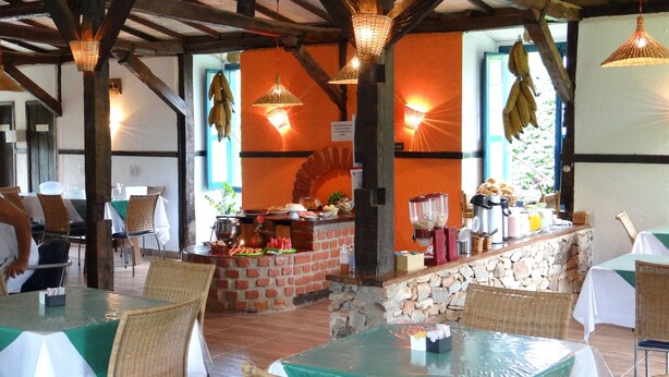An outdoor dining area with brick walls, wicker chairs, and tables covered with green tablecloths. - Pousada Banana Cipó (Santana do Riacho)