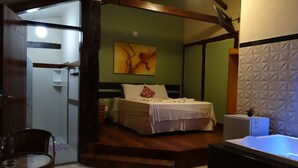 A bedroom with a bed, a nightstand, a chair, a desk, and a bathroom with a sink and mirror. - Pousada Banana Cipó (Santana do Riacho)