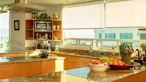 A modern kitchen with granite countertops, wooden cabinets, a microwave, and a large window offering a view of the outdoors. - Ph Toshi (Puerto Vallarta)