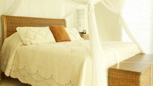 A bedroom with a four-poster bed, a nightstand, and a wicker side table. - Ph Toshi (Puerto Vallarta)
