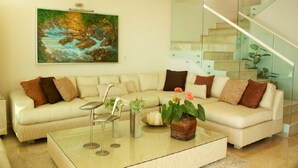 A modern living room with a beige sectional sofa, a glass staircase, and a painting of a landscape. - Ph Toshi (Puerto Vallarta)
