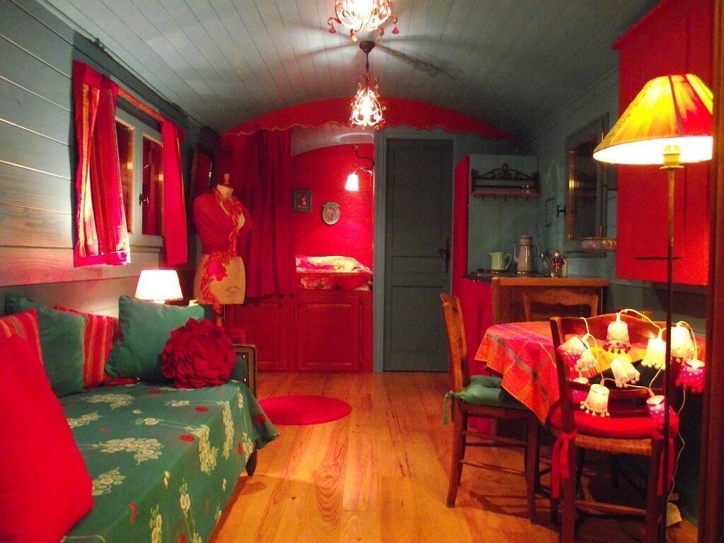 Una habitación acogedora con suelo de madera, un sofá verde con tapizado floral, una mesa de comedor con mantel rojo y una lámpara de araña.