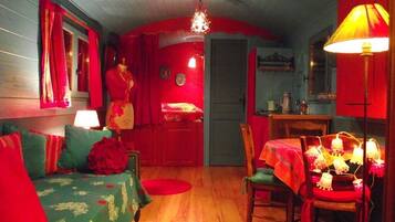 Una habitación acogedora con suelo de madera, un sofá verde con tapizado floral, una mesa de comedor con mantel rojo y una lámpara de araña.
