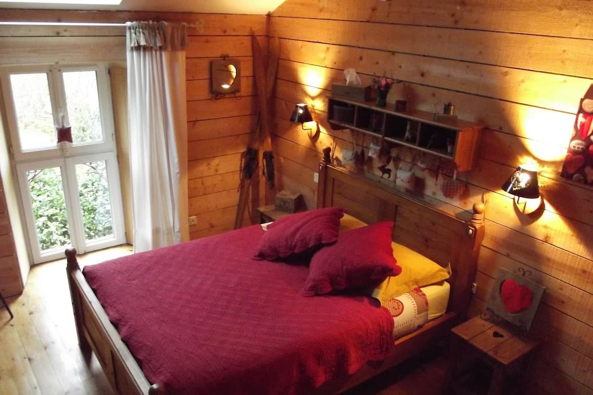 A wooden room with a bed, a window, and a shelf with various items.