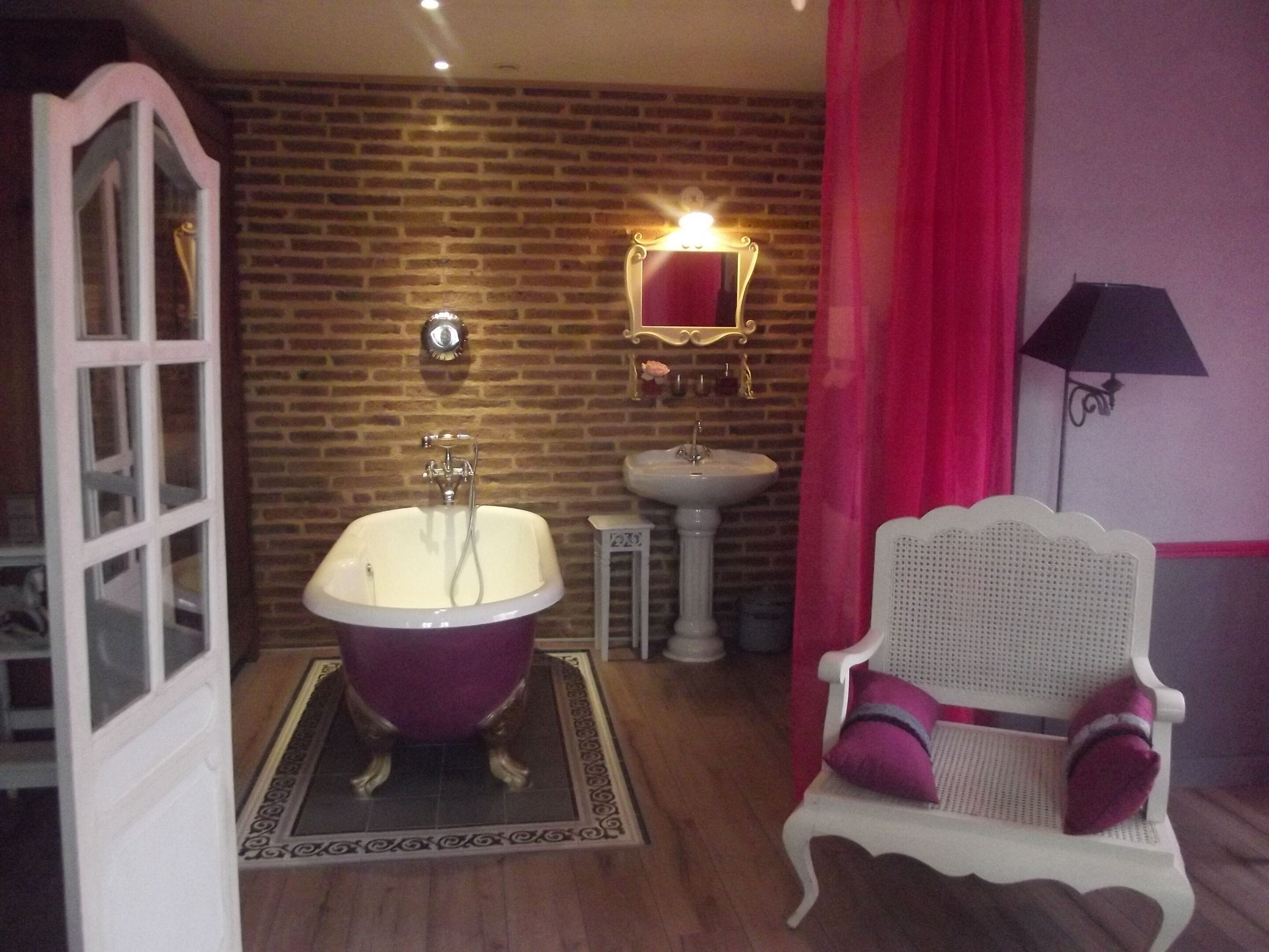 A bathroom with a freestanding bathtub, a pedestal sink, a mirror, and a white chair with a cushion.