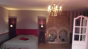 A bedroom with a bed, two bedside lamps, a chandelier, a brick fireplace, and a white door. - Chambres d'hôtes La Chaussée d'Olivet (Olivet)