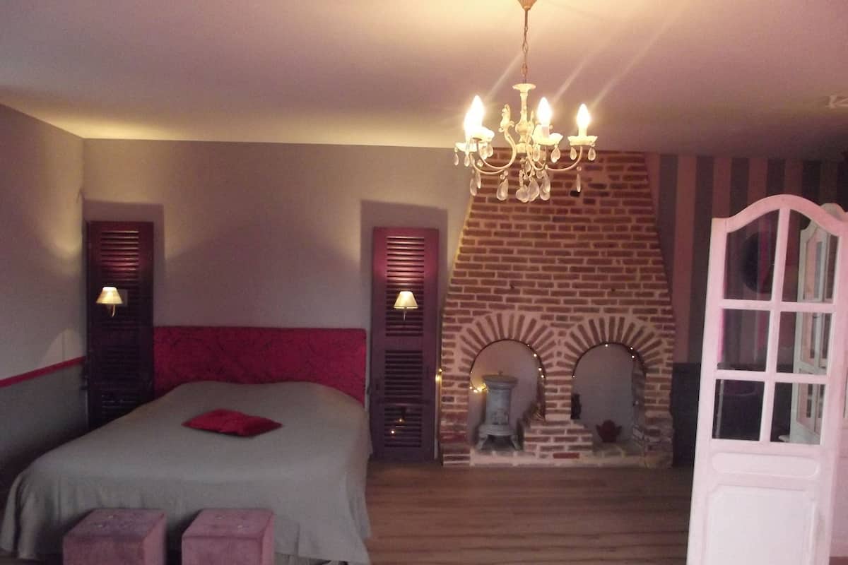A bedroom with a bed, two bedside lamps, a chandelier, a brick fireplace, and a white door.