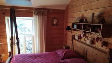 Ein Zimmer aus Holz mit einem Bett, einem Fenster mit Vorhängen und einem Regal mit herzförmigen Dekorationen.