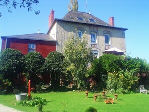A large two-story house with a well-maintained garden, including a lawn, potted plants, and outdoor furniture. - Chambres d'hôtes La Chaussée d'Olivet (Olivet)