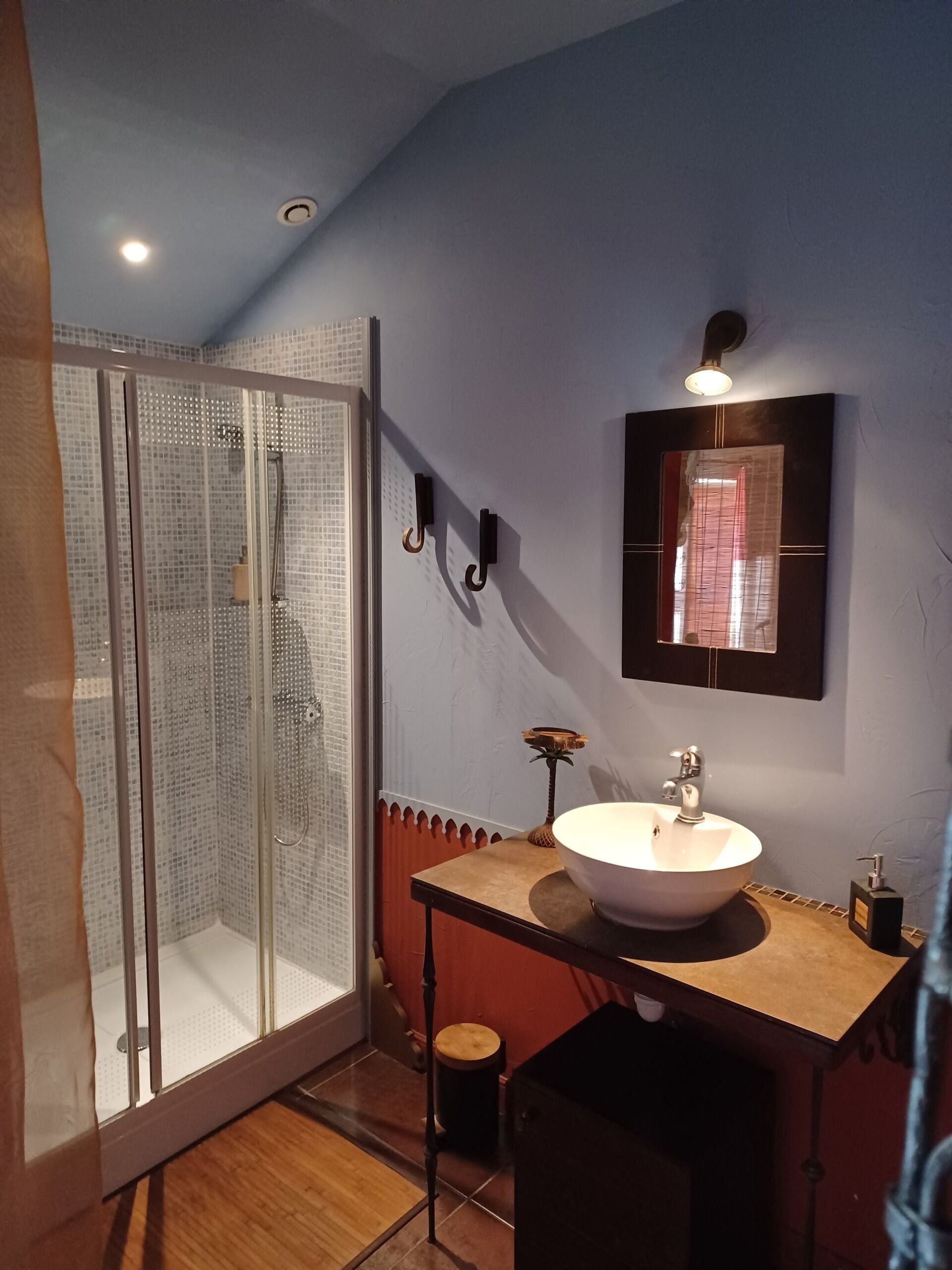 Un baño con cabina de ducha de vidrio, un lavamanos con espejo y un taburete pequeño.