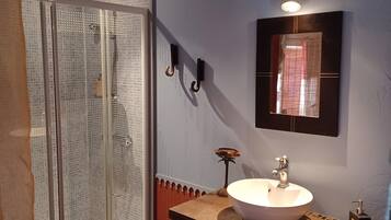 Un baño con cabina de ducha de vidrio, un lavamanos con espejo y un taburete pequeño.