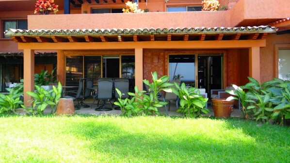 A covered outdoor seating area with chairs and tables, surrounded by potted plants and a grassy lawn. - Unlimited Luxury Villa  LOS TULES (Puerto Vallarta)
