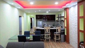 A compact kitchen with a dining area, featuring a central island, wooden chairs, and a refrigerator. - Unlimited Luxury Villa  LOS TULES (Puerto Vallarta)